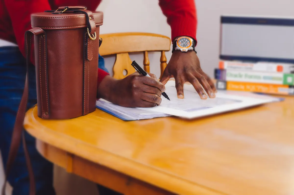 Hands writing on a document at a wooden desk, representing property management terms and conditions